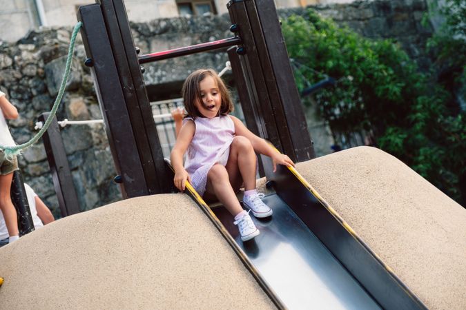 Cautious curios girl rolling down slide at playground