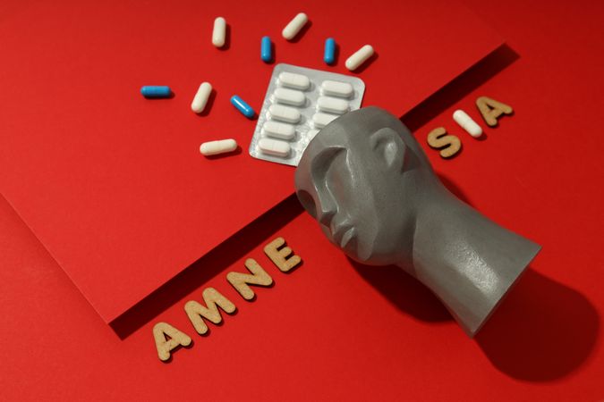 Bust with pills on red background and the words “Amnesia” copy space