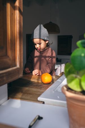 Cute child peeling citruses at table in kitchen