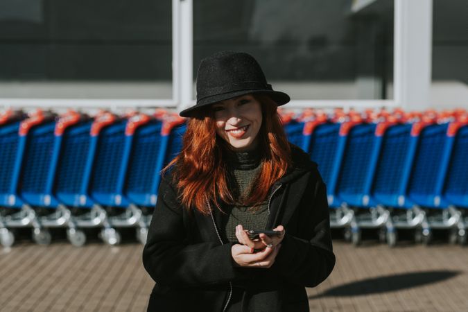 Smiling woman with smartphone in parking lot with shopping carts