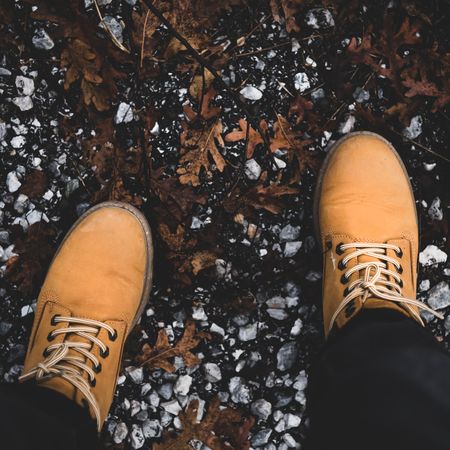 Heavy boots against a autumn path with fallen leaves and stones, square crop