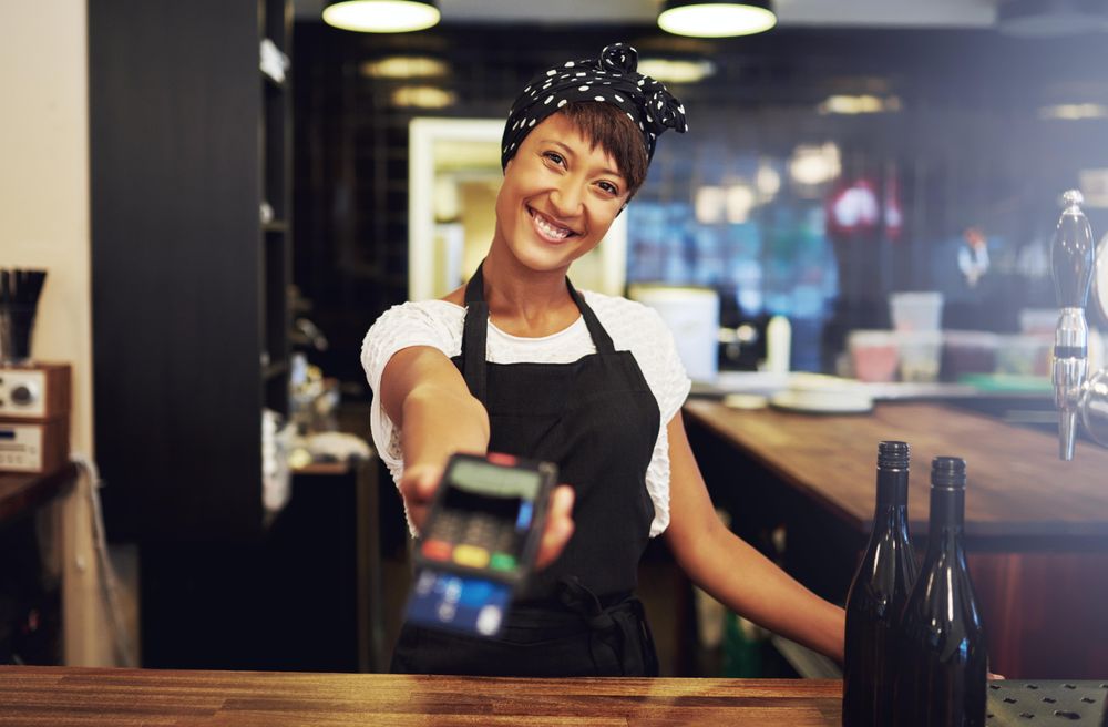 Black woman passing over credit card machine from behind bar