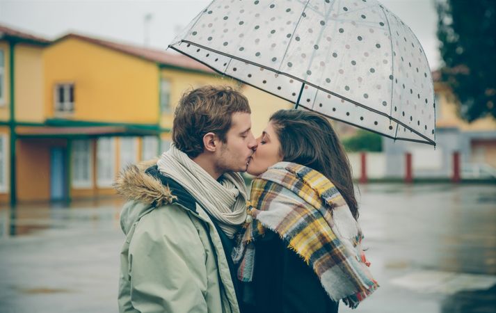 Boyfriend and girlfriend kissing under dotted umbrella on rainy day
