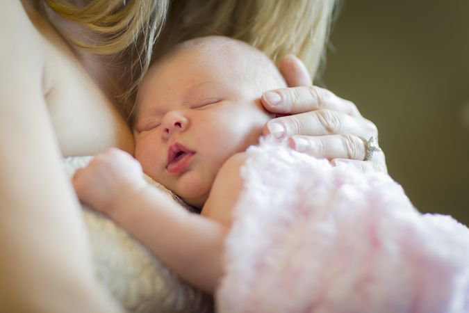 Hands of Mother Holding Her Newborn Baby Girl To Her Chest