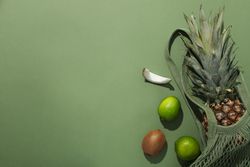 Tropical fruit in bag on green background, space for text