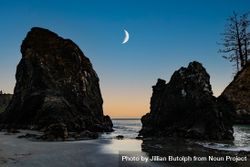 Crescent moon between two large rocks on quiet beach at dusk 5RlDDb