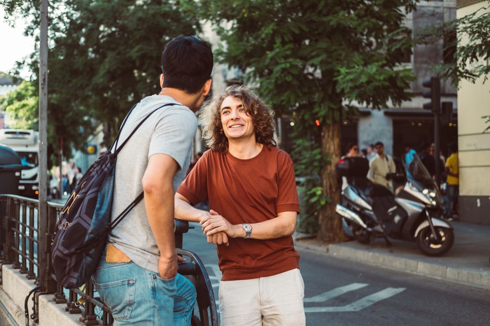 Cool multiracial male friends chatting while standing on street