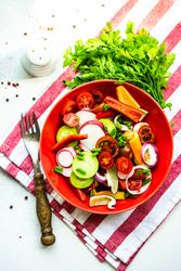 Top view of colorful healthy raw vegetable salad served in red bowl on red striped napkin