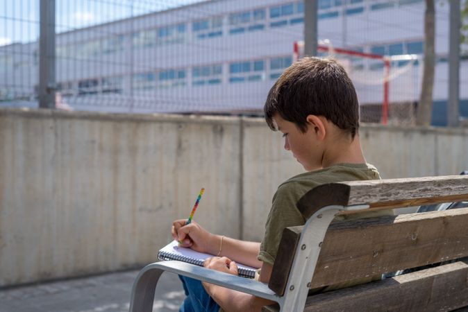 Boy sitting on bench writing in note book
