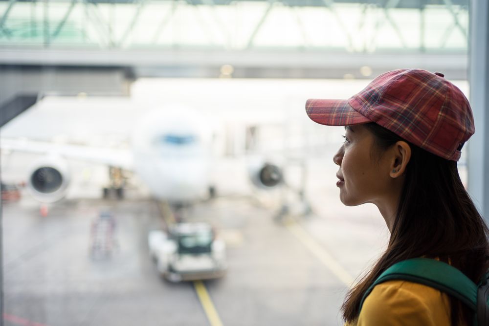 Smiling Asian woman looking down through window at runway with plane