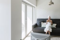 Happy relaxed woman enjoying day off while having hot drink after shower and watching TV in apartment in loft style