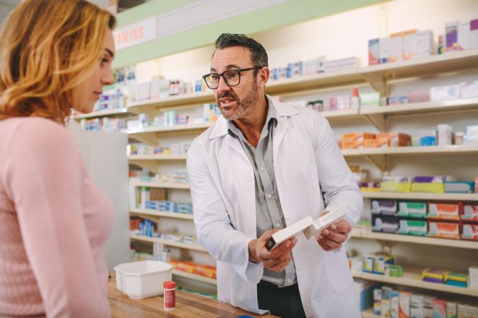 Male pharmacist holding medicine box giving advice to female customer in chemist shop