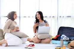 Two Asian Friends Discuss Vacation Ticket Payments While Packing Their Suitcases