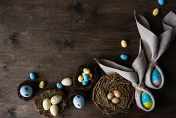 Easter eggs wrapped with rabbit ears with napkin with bird nests on wooden table