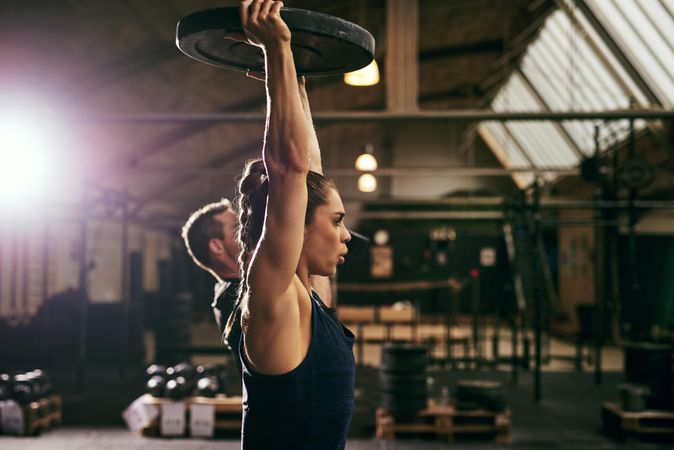 Strong woman lifting heavy weight plate above her head