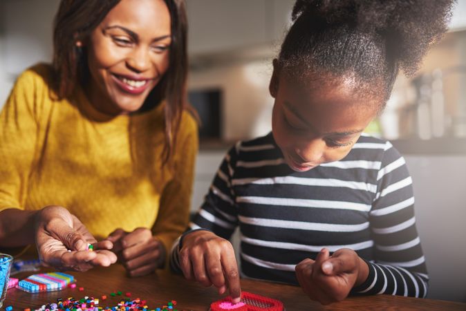 Smiling Black mother and daughter doing arts and crafts with beads at home