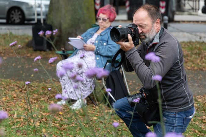 Man taking photograph in field with woman drawing behind him