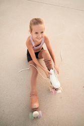 Child lacing up roller skates while sitting on concrete ground