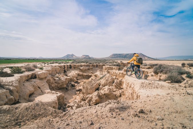 Man with bicycle standing on stone in desert hills