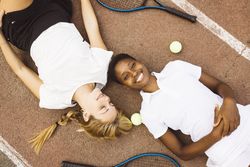 Portrait of two women laying on a tennis court.