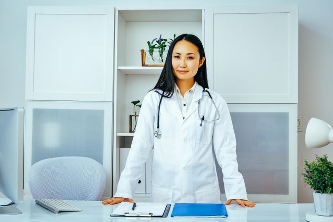 Confident Asian doctor at work standing behind her desk