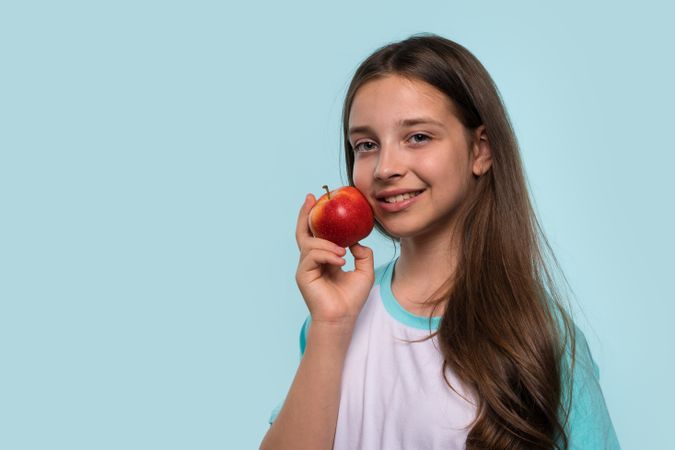 Girl smiles while holding red apple against her cheek