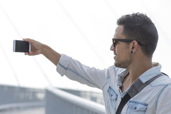 Man in denim shirt standing outside taking photo with phone
