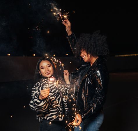 Asian and Black woman celebrating at night with sparklers