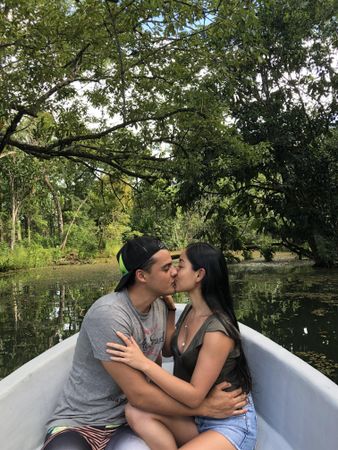 Man and woman kissing while sitting in boat in river surrounded by tree