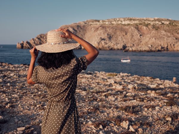 Unrecognizable woman standing on seashore and looking at boat