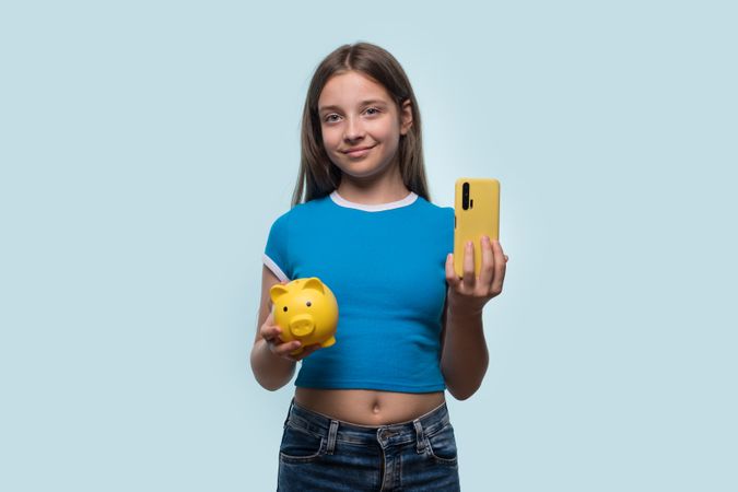 Girl holding yellow piggy bank and smartphone