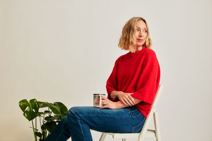 Blonde woman in red sweater sitting in a chair holding coffee mug inside