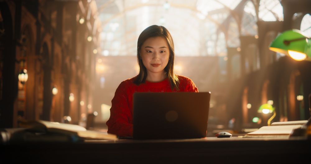 Dedicated Asian Female Student Engaged in E-Learning Using Laptop in Classical Library Setting