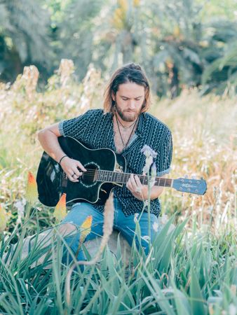 Hipster man in meadow with guitar