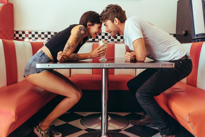 Romantic couple sharing a milk shake with two straws while looking at each other at a restaurant