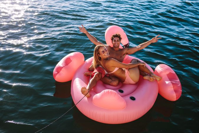 Happy man and woman sitting on inflatable toy tied to boat