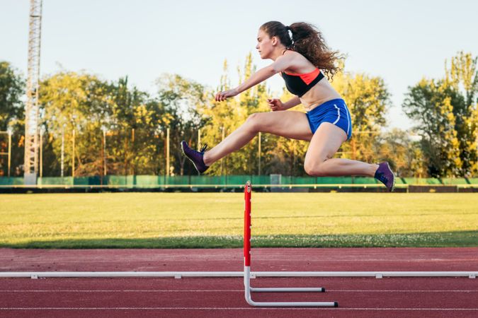 An athletic woman jumping hurdles on an athletics track.