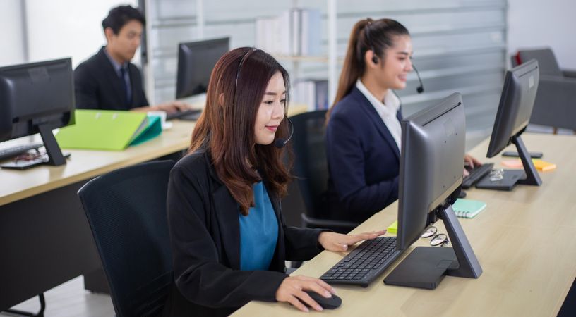 Young Asian business call center employees with headset sitting in office