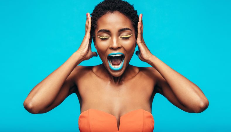 Woman with colorful makeup screaming against blue background
