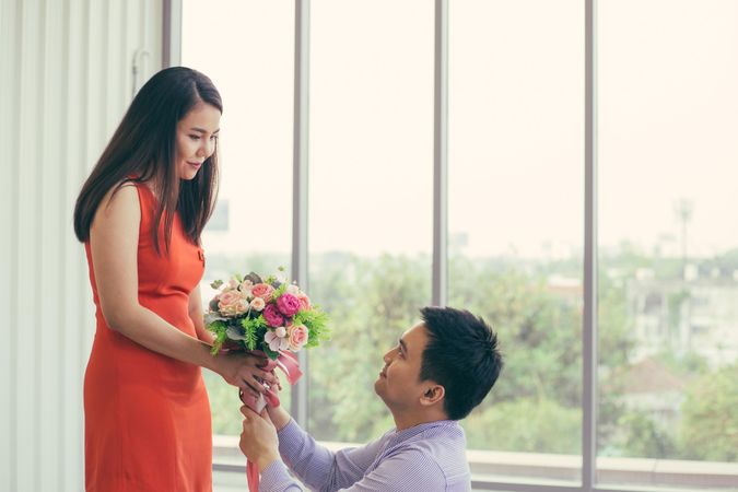 Male with bouquet of flowers kneeling before female in red dress