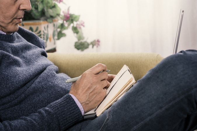 Close-up of a man writing in a notebook at home.