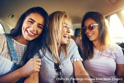 Group of smiling female friends laughing with each other while riding in back of vehicle bDB1k5