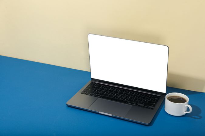 Open laptop with blank mockup screen in cream and blue room with cup and copy space