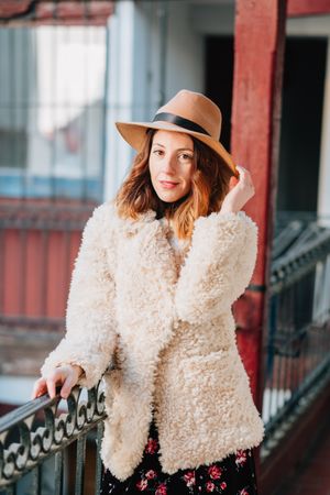 Smiling woman in warm wear standing near building and fence