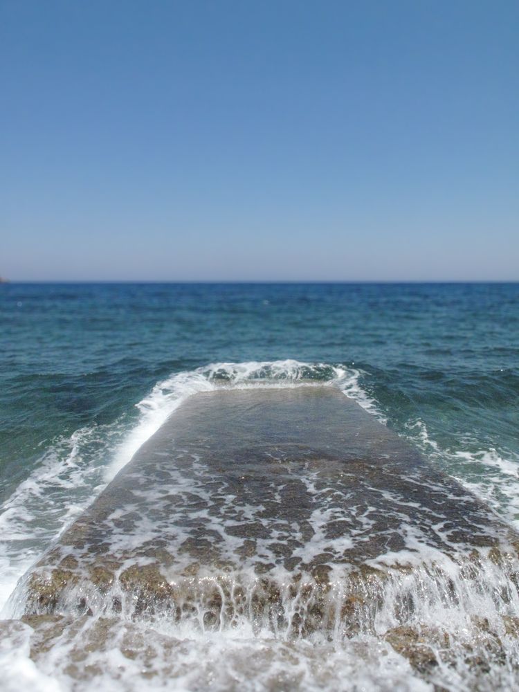 Seawater washes over broken stone jetty at Lampi beach, Patmos