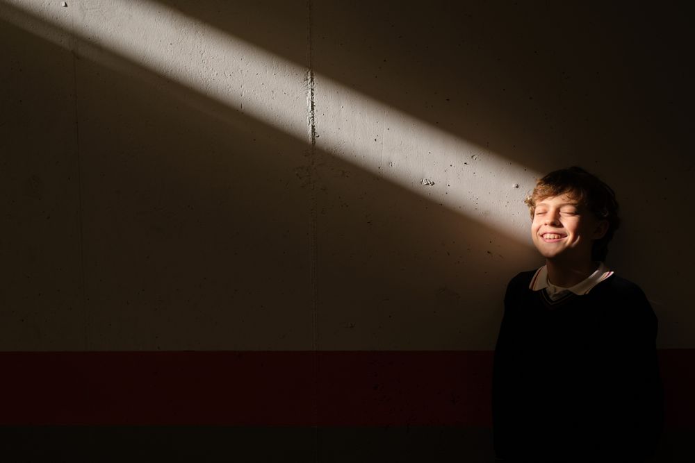 Smiling boy standing with closed eyes at wall in sunbeam