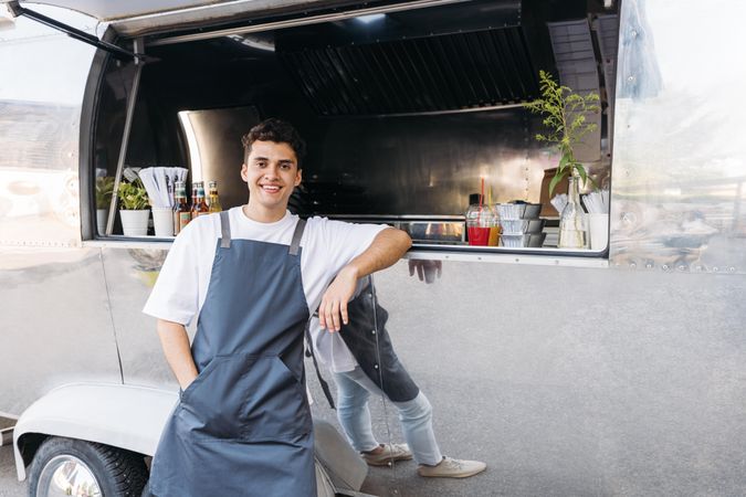 Proud male in apron and leaning on open counter of food truck