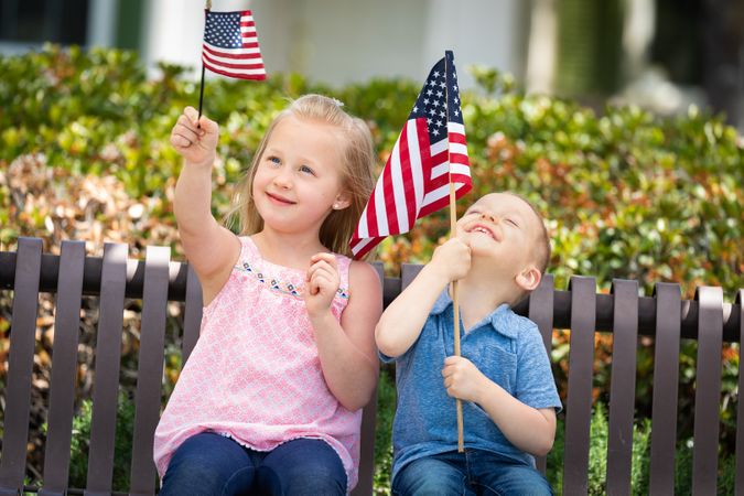 Young Sister and Brother Comparing Each Others American Flag Size On The Bench At The Park