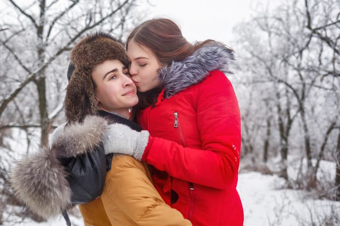 Teenage girl kissing boyfriend in wintery forest