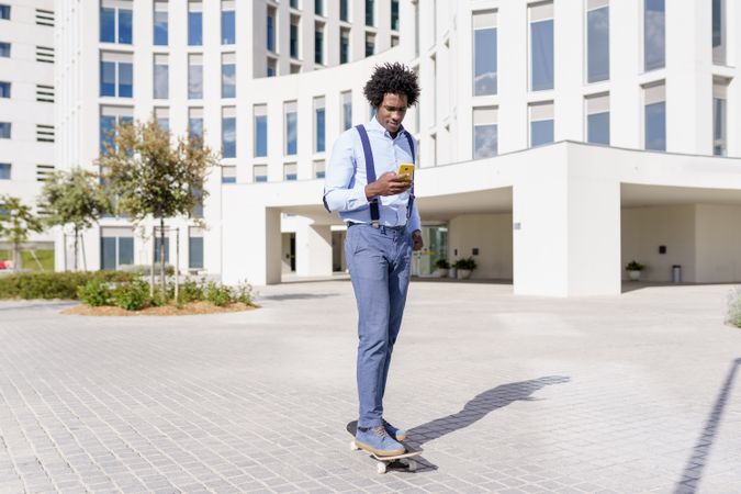 Man on skateboard checking phone outside office